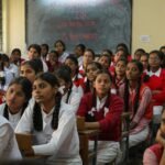 Group of Indian schoolgirls in uniform attentively listening in a classroom setting.